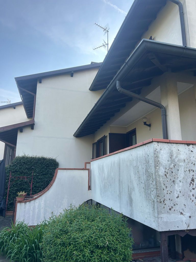Vista laterale di un edificio residenziale con balcone e vegetazione intorno, prima dell'intervento di ripristino.