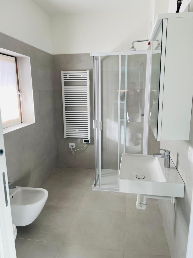 Interno di un bagno moderno con piastrelle grigie, doccia in vetro, lavabo e bidet.