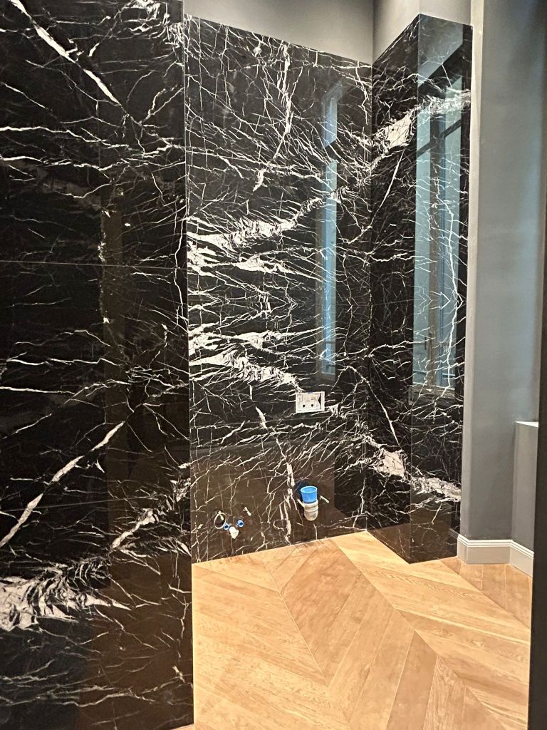 Doccia elegante con pareti in marmo nero e bianco, pavimento in legno a spina di pesce.