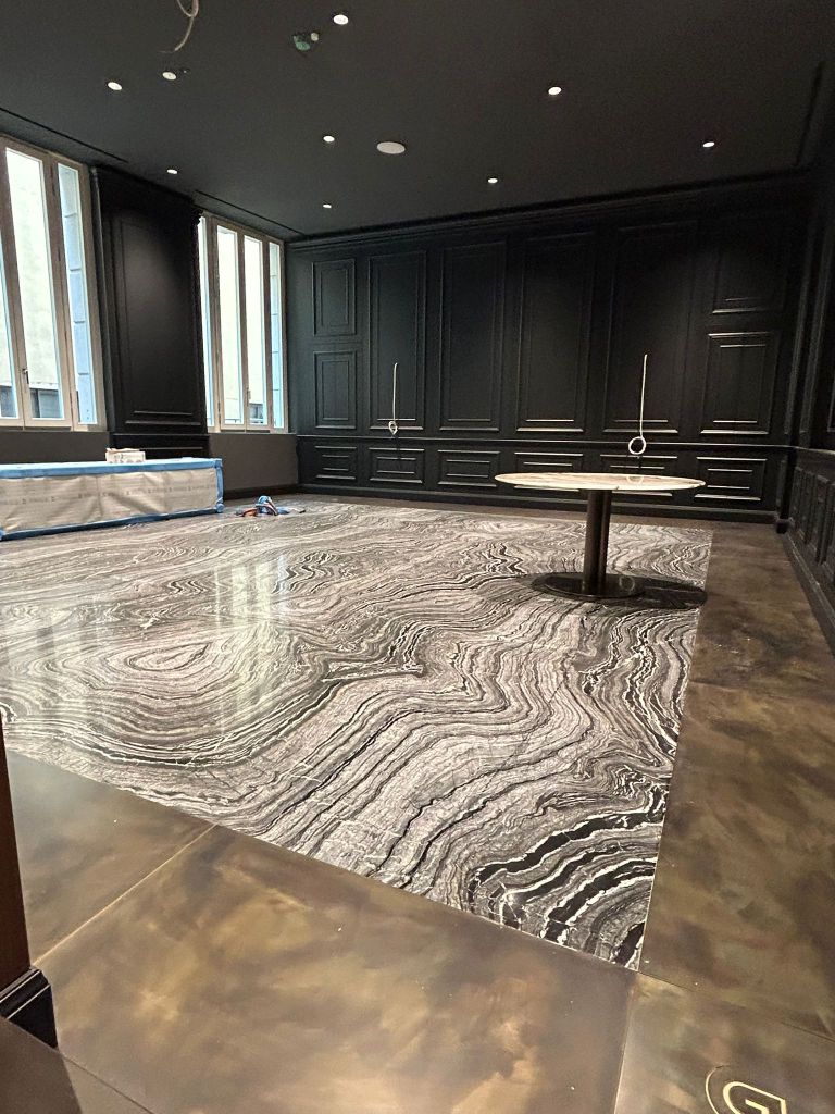 Interno di una stanza con pareti nere, pavimento in marmo decorato con venature grigie e bianche, e un tavolo circolare al centro.