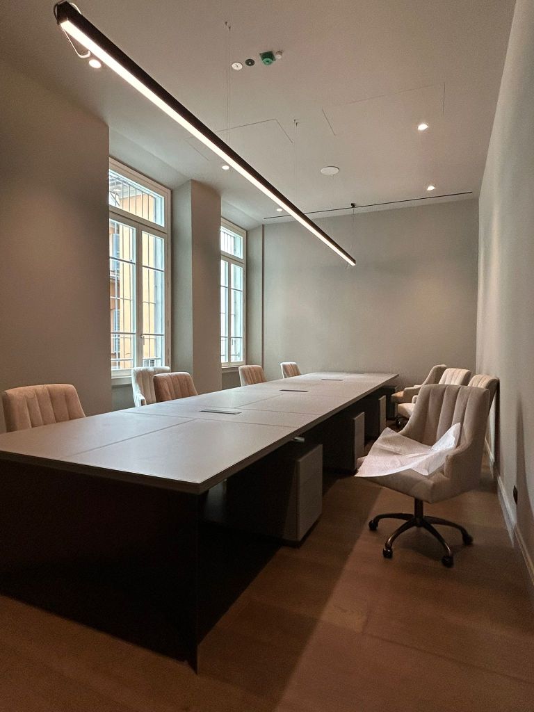 Sala riunioni moderna con un grande tavolo ovale e sedie imbottite, illuminata da un'illuminazione a soffitto.