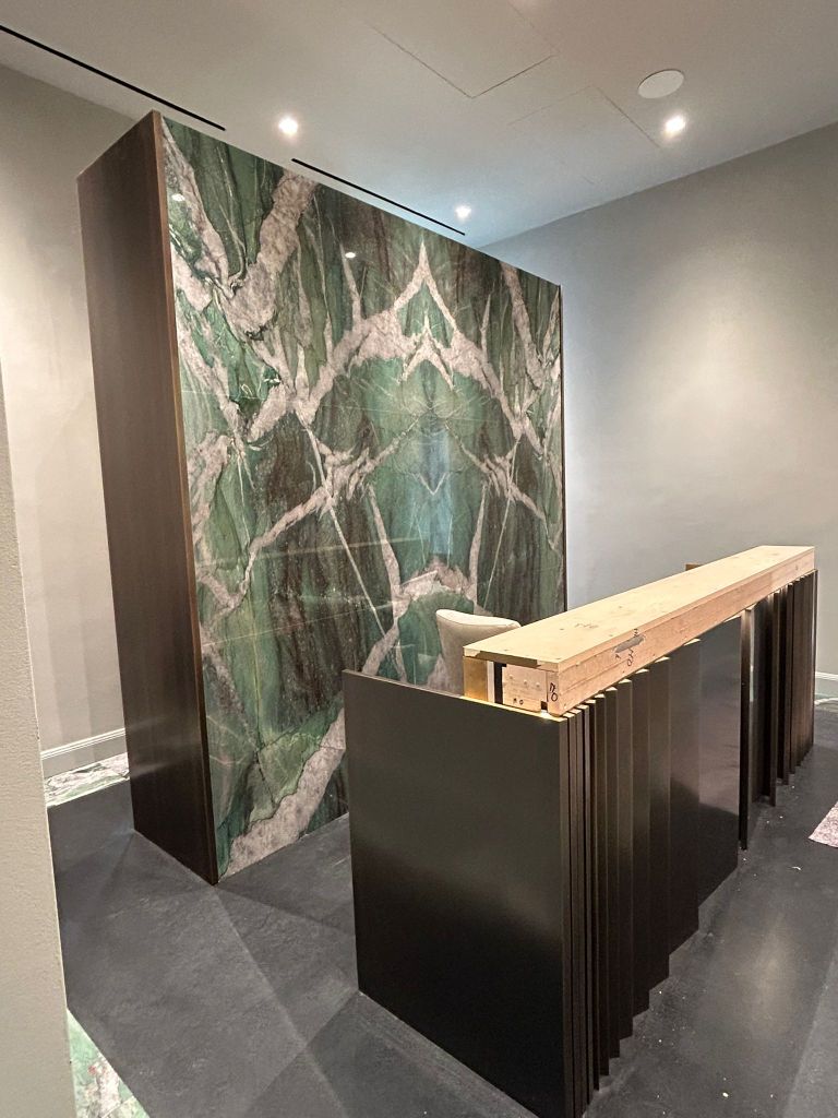 Reception con parete in marmo verde e bancone in metallo nero.